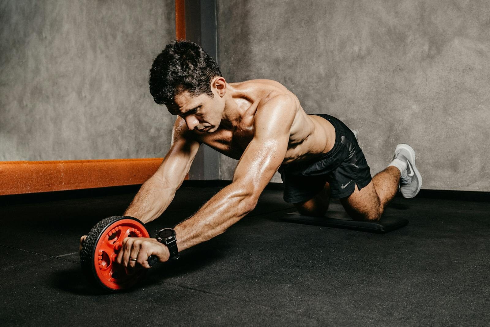 Muscular man exercising with an ab roller for core strength in an indoor gym setting, showcasing athletic fitness.